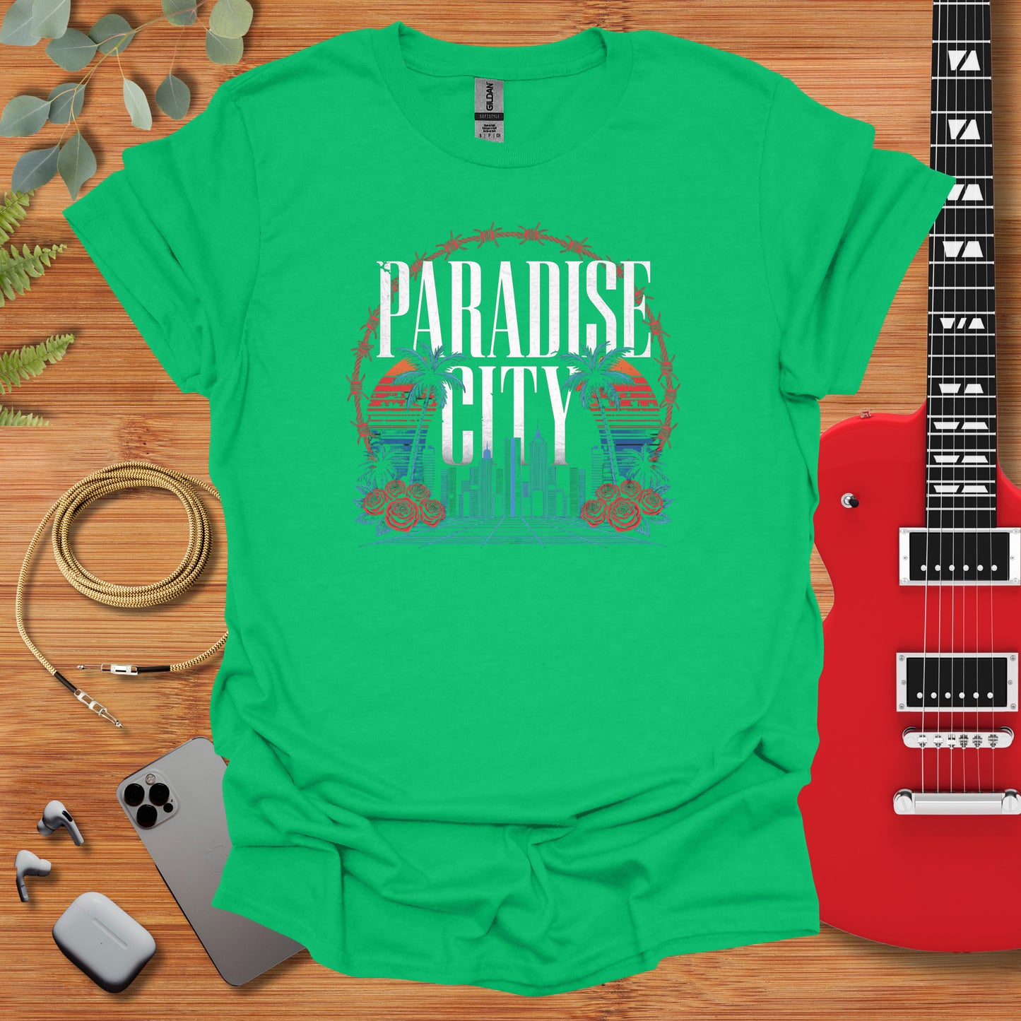 a green t - shirt with the phrase paradise city on it next to a guitar