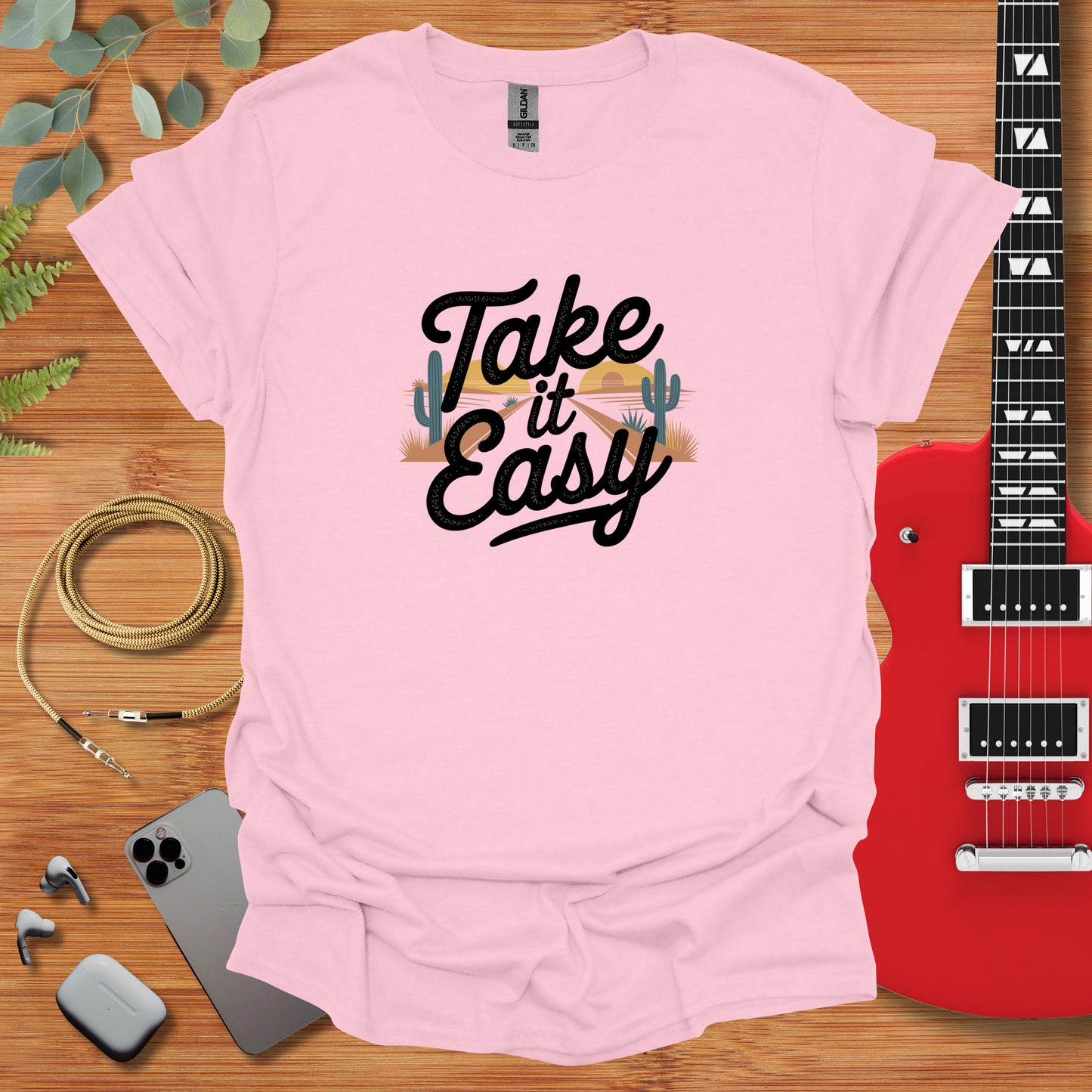 a pink shirt that says take it easy next to a guitar