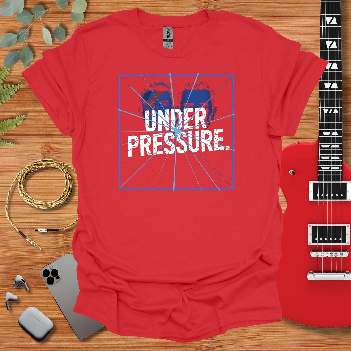 a red shirt with the words under pressure on it next to a guitar