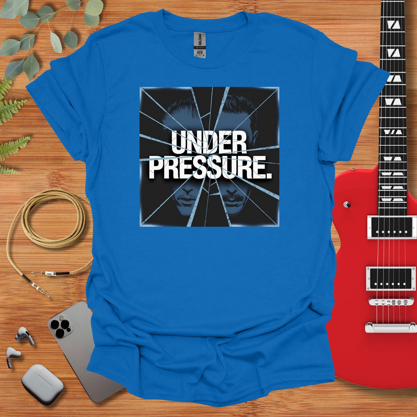 a blue t - shirt with the words under pressure on it next to a guitar