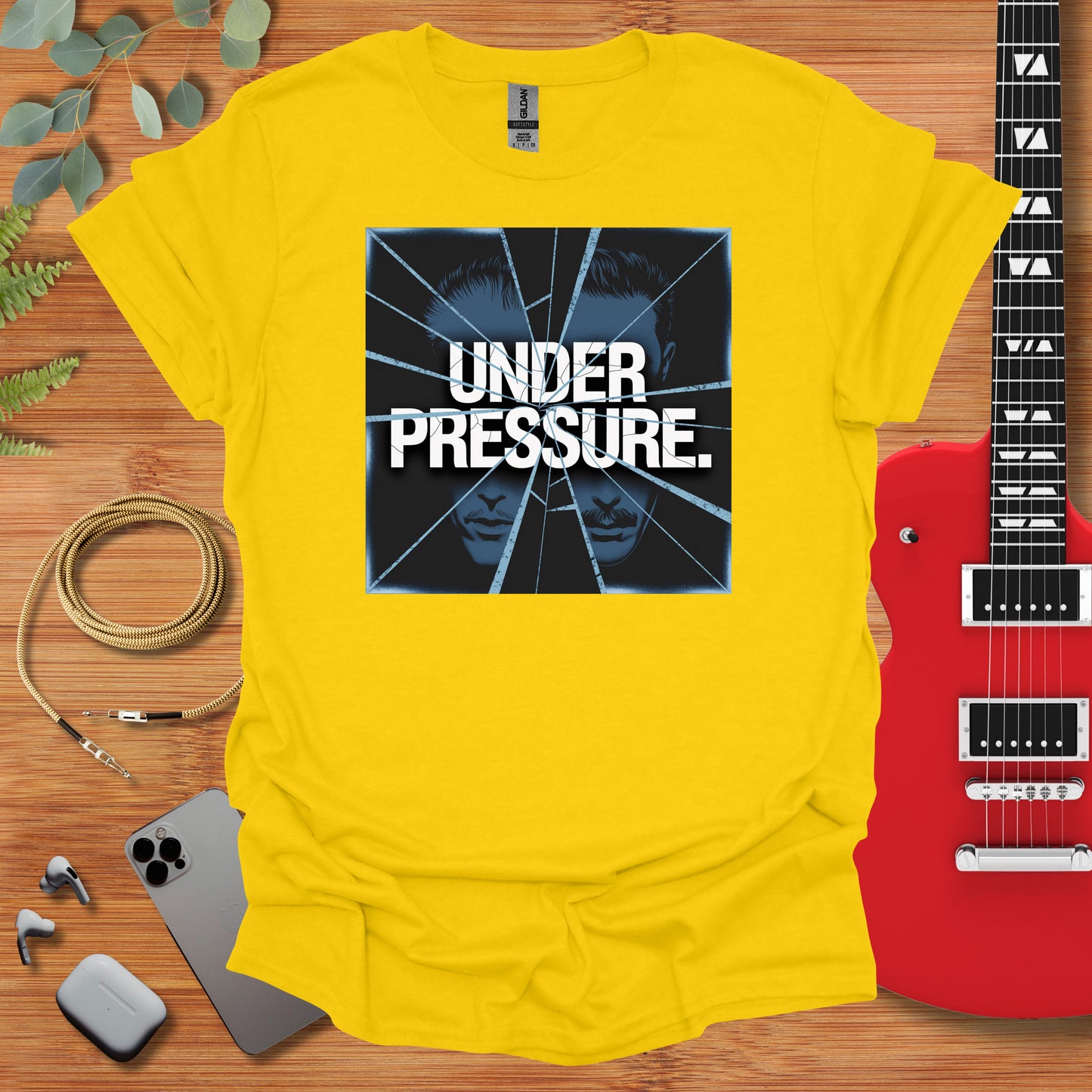 a yellow t - shirt with the words under pressure on it next to a guitar